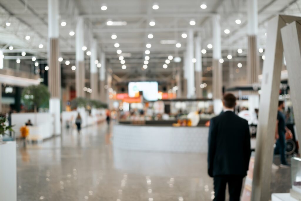 Defocused shopping mall background, large illuminated hall, Retail Security Guard rear view. Blurred