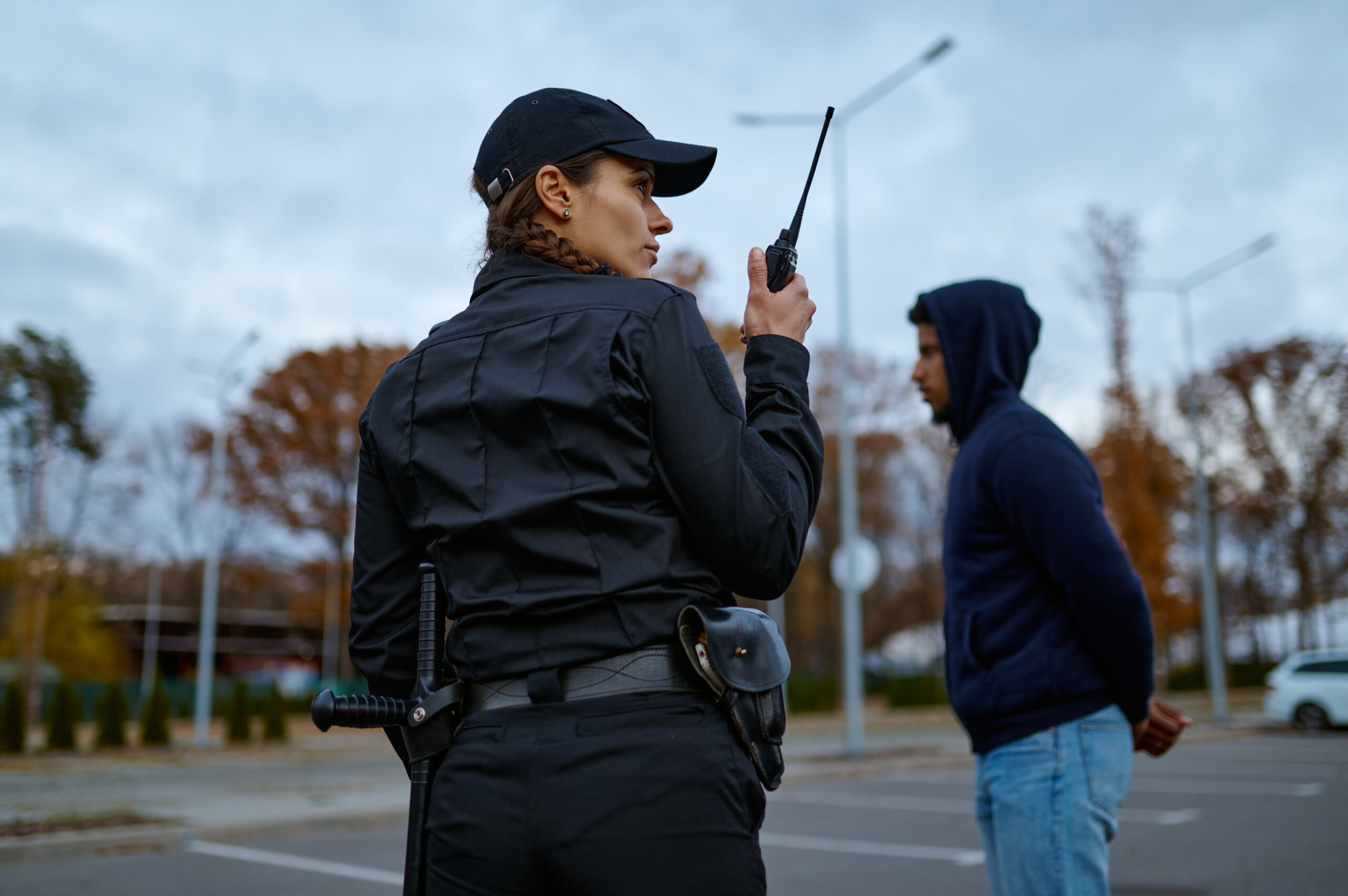 View from back on woman cop in uniform using portable radio for police communication