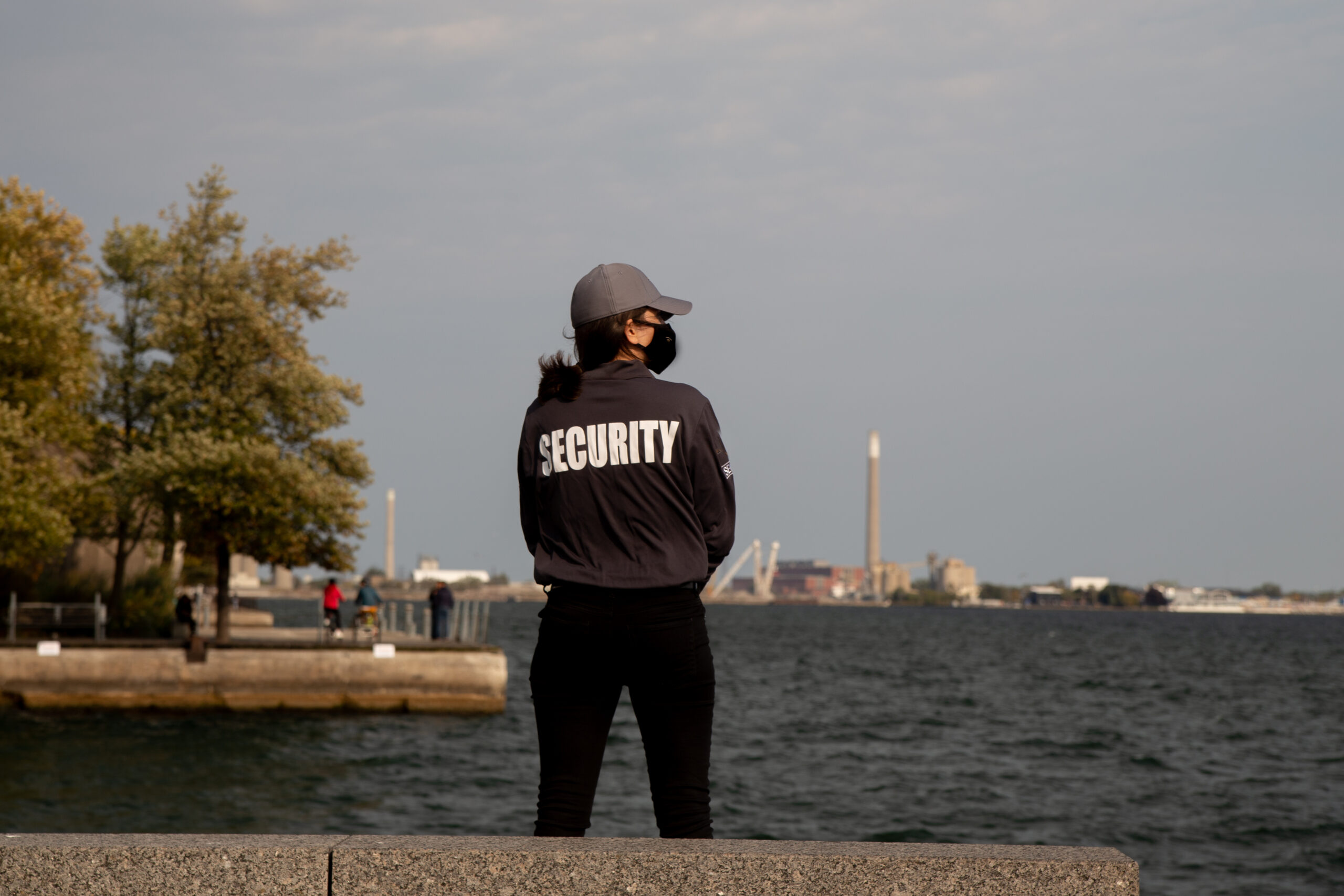 A closeup shot of a female security guard in uniform and mask watching over the harbor area