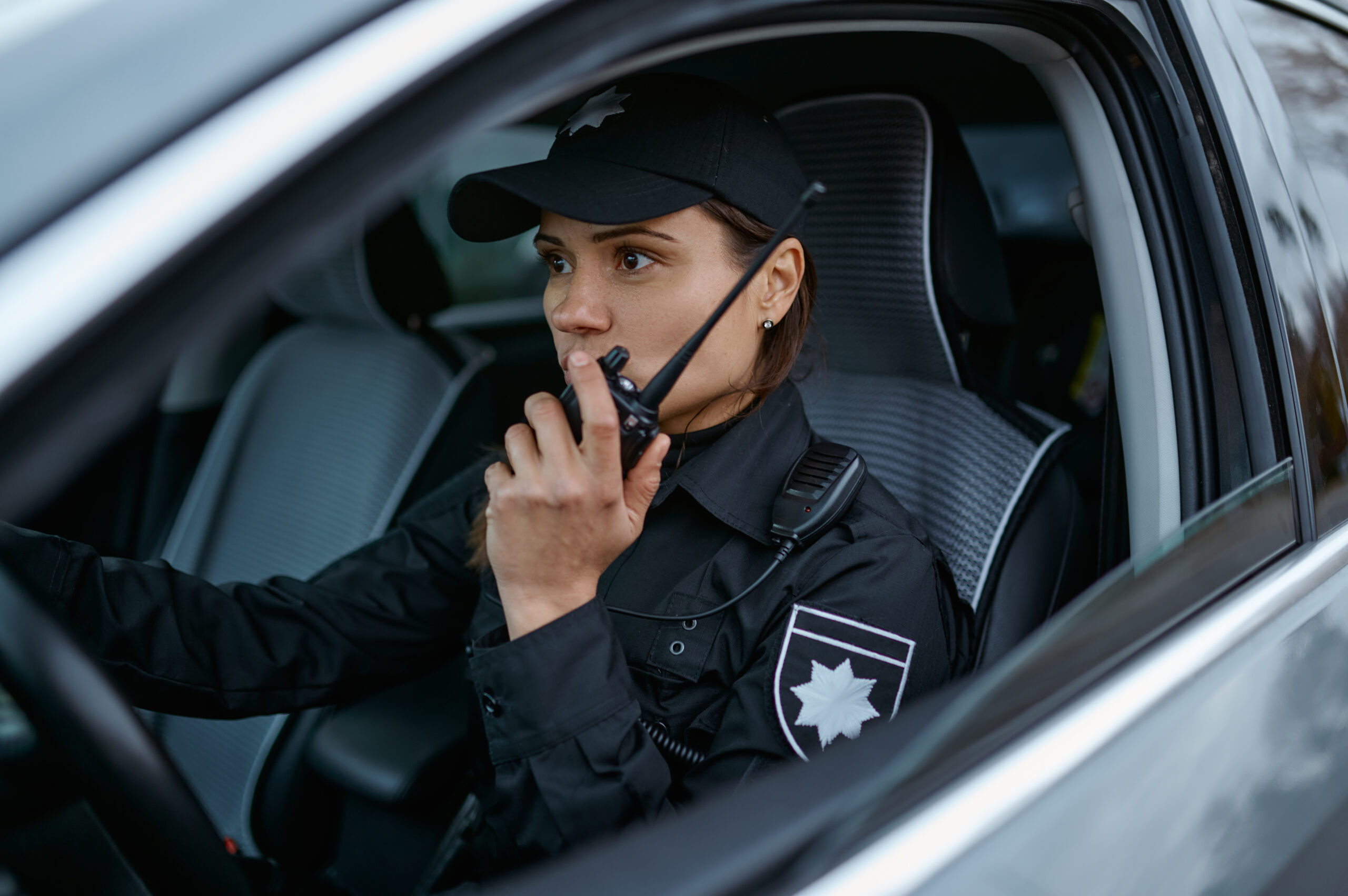 Woman police officer using walkie-talkie portable radio driving in car. Female cop patrolling street
