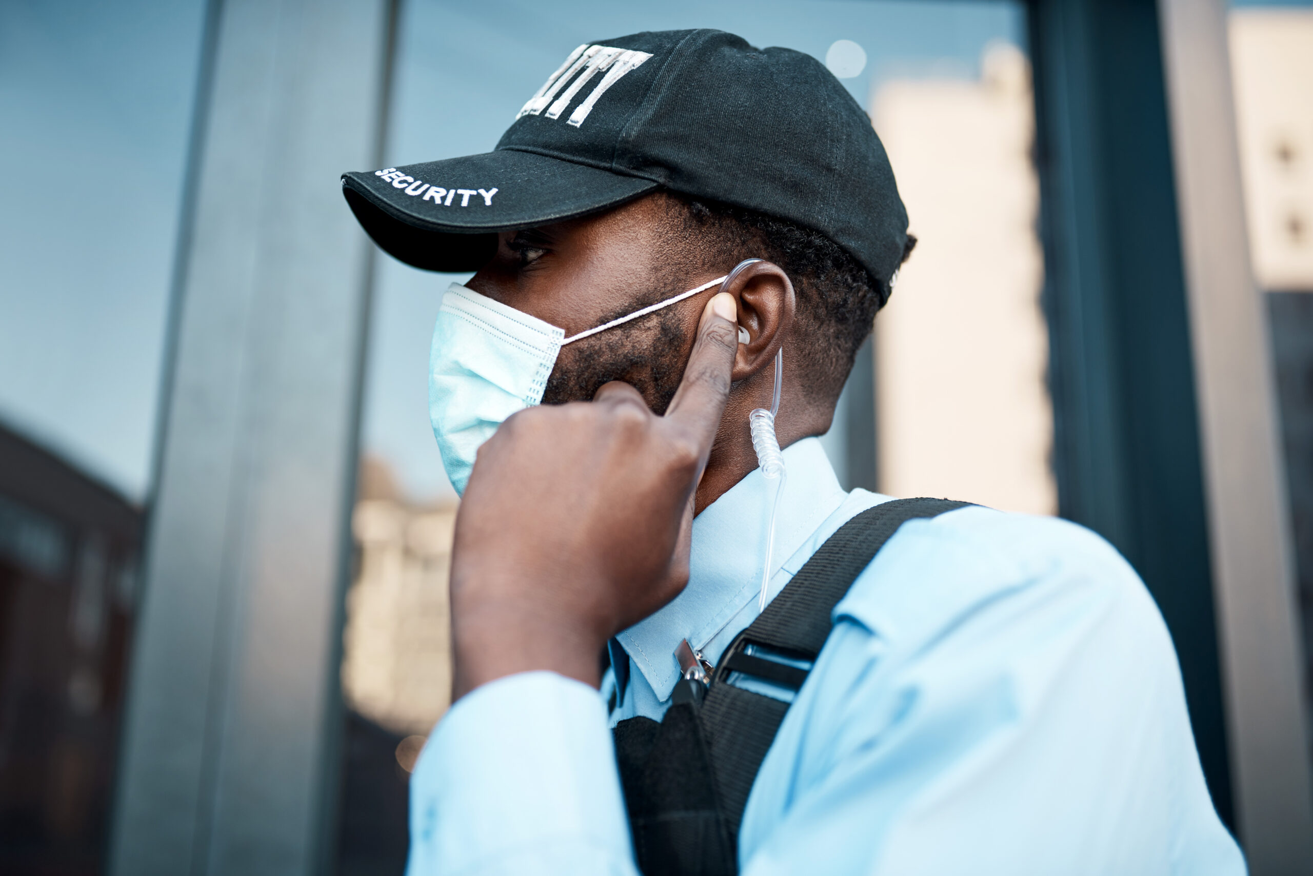 Shot of a masked young security guard using an earpiece while on patrol outdoors.