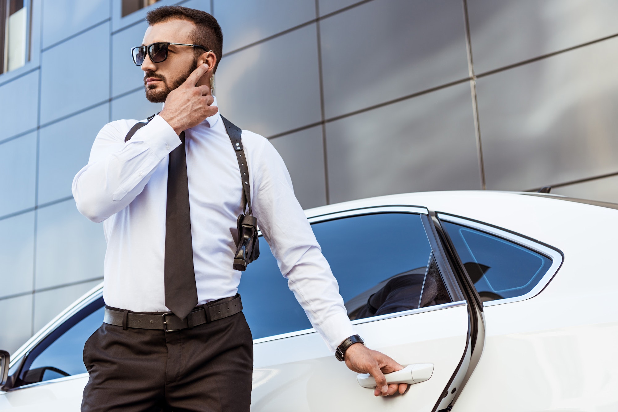 Handsome security guard listening message with security earpiece on street and opening car