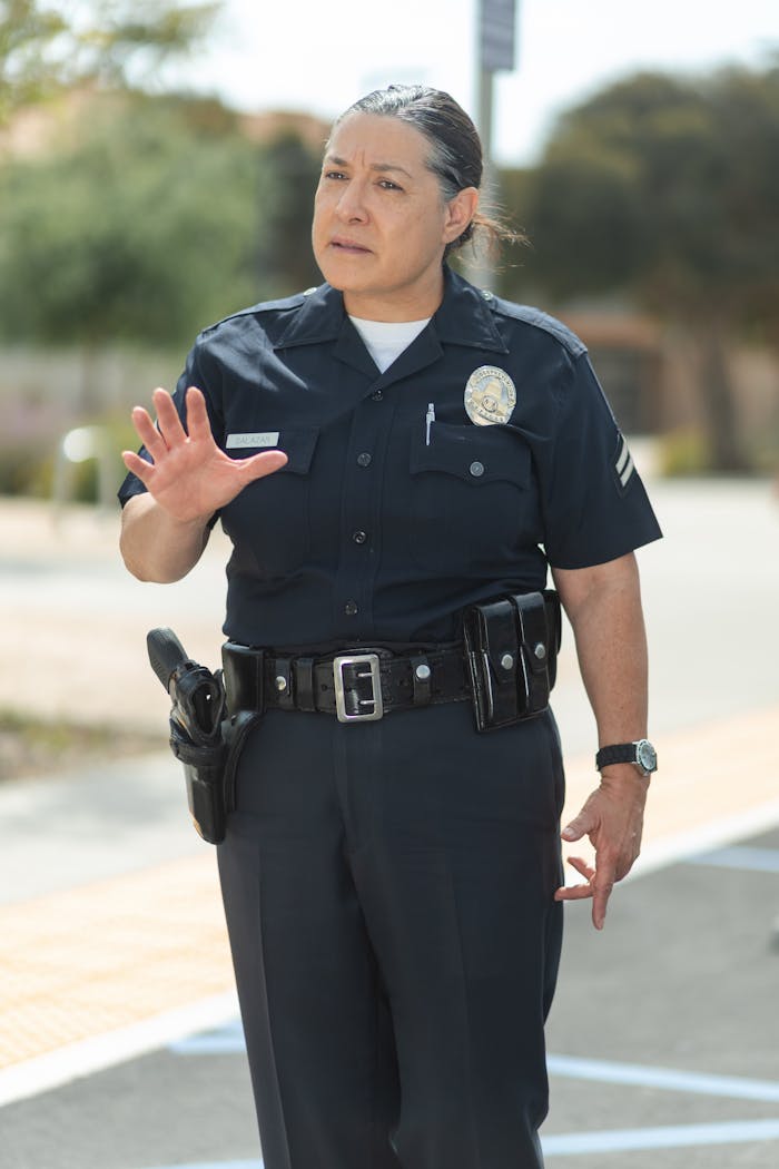 Experienced female police officer gesturing for attention in a city setting.
